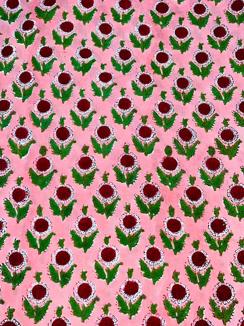 May include: Pink fabric with a repeating pattern of white and red flowers with green leaves.