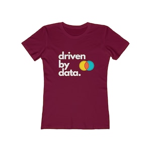 Pode incluir: Uma camiseta feminina vinho com o texto "driven by data." em letras brancas. O texto é acompanhado por um gráfico de dois círculos sobrepostos, um amarelo e outro azul.