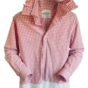May include: A long-sleeved button-down shirt in a pink and white gingham check pattern. The shirt features a large ruffled collar, a single chest pocket, and a white eyelet lace trim along the bottom hem. A label reads REFALLLACK.