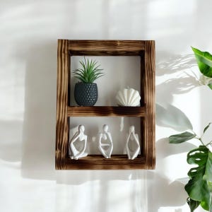 May include: A rustic wooden shelf with two tiers, featuring a small potted plant, a white seashell, and three white ceramic figurines. The shelf is mounted on a white wall.