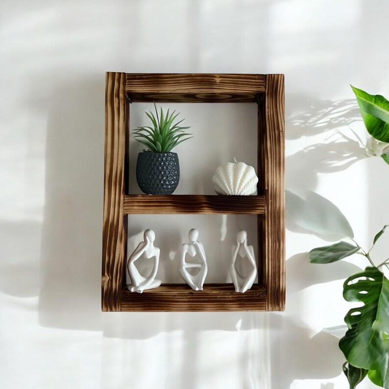 May include: A rustic wooden shelf with two tiers, featuring a small potted plant, a white seashell, and three white ceramic figurines. The shelf is mounted on a white wall.