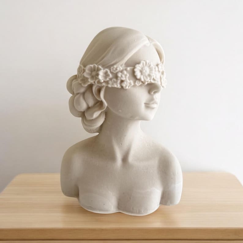 Puede incluir: Busto de mujer de yeso blanco con una venda de flores blancas.