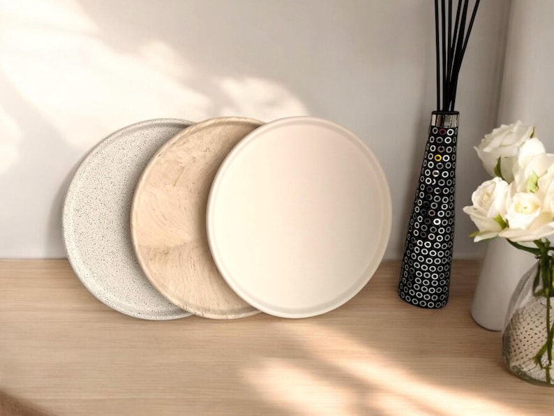 May include: Three round trays, one white, one beige, and one speckled with white on a beige background. The trays are stacked on top of each other.