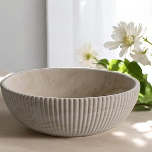 May include: A large, white, ribbed ceramic bowl. The bowl is made of a textured material and has a smooth, rounded interior.