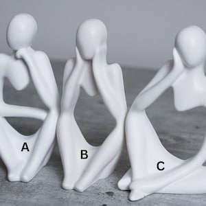 May include: Three white ceramic sculptures of abstract figures in a seated pose. Each figure has its head resting on its hand, and the figures are labeled A, B, and C.
