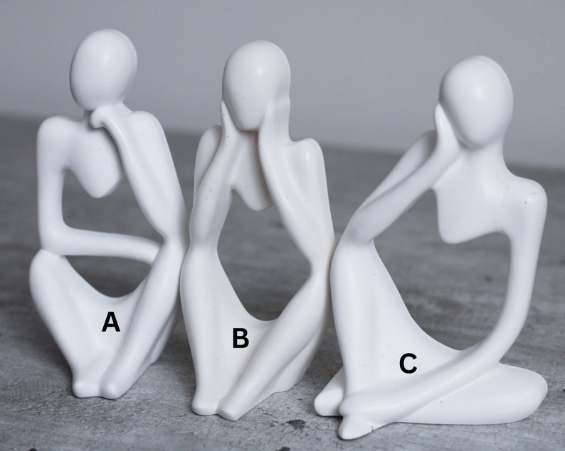 May include: Three white ceramic sculptures of abstract figures in a seated pose. Each figure has its head resting on its hand, and the figures are labeled A, B, and C.