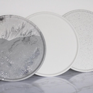 May include: Three round concrete trays with different finishes. One tray has a white speckled finish, one has a white finish, and one has a gray and white marbled finish.