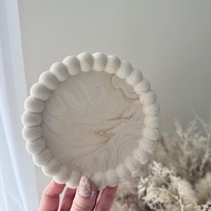 May include: A white round tray with a beaded edge. The tray has a marbled design with white and brown swirls.