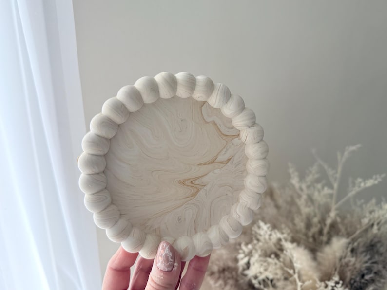 May include: A white round tray with a beaded edge. The tray has a marbled design with white and brown swirls.