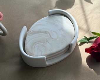 May include: A set of four white ceramic coasters with a marbled design. The coasters are in a white ceramic holder.