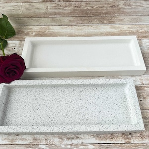 Op de afbeelding: Twee rechthoekige trays, &eacute;&eacute;n wit en &eacute;&eacute;n met een gespikkelde witte en grijze afwerking. De trays zijn gemaakt van een glad, stevig materiaal.