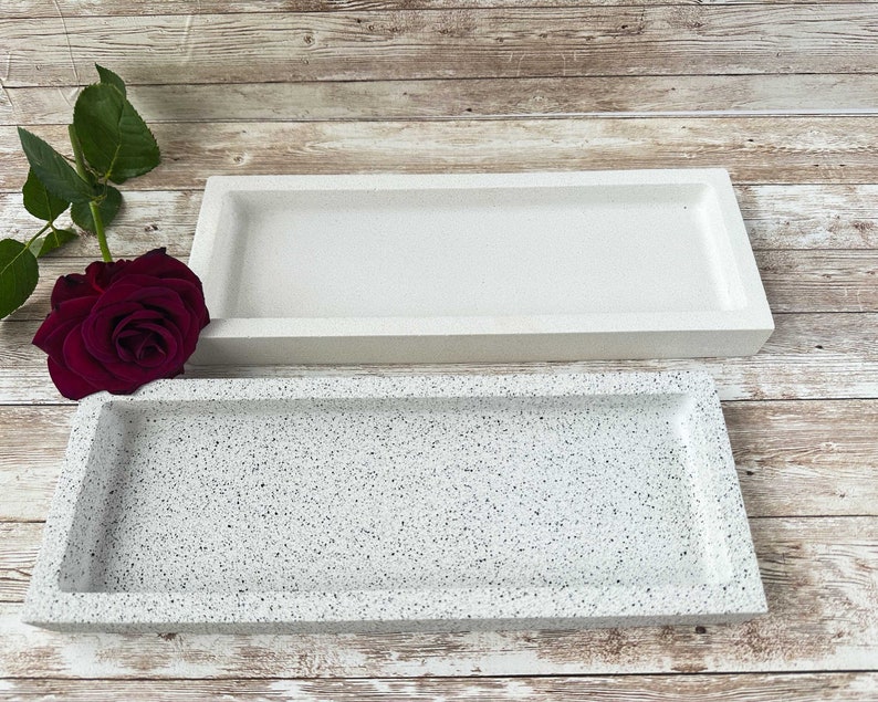 Op de afbeelding: Twee rechthoekige trays, &eacute;&eacute;n wit en &eacute;&eacute;n met een gespikkelde witte en grijze afwerking. De trays zijn gemaakt van een glad, stevig materiaal.