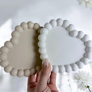 May include: Two heart-shaped coasters with a raised bubble texture. One coaster is beige and the other is white.