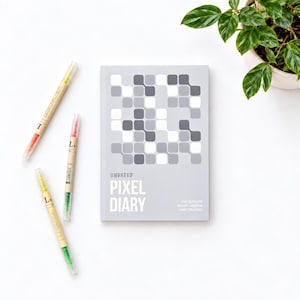 May include: A grey undated pixel diary journal with a white geometric pattern of rounded squares on the cover, featuring the text Undated Pixel Diary and The Ultimate Bullet Journal Habit Tracker, accompanied by three double-ended coloured markers.