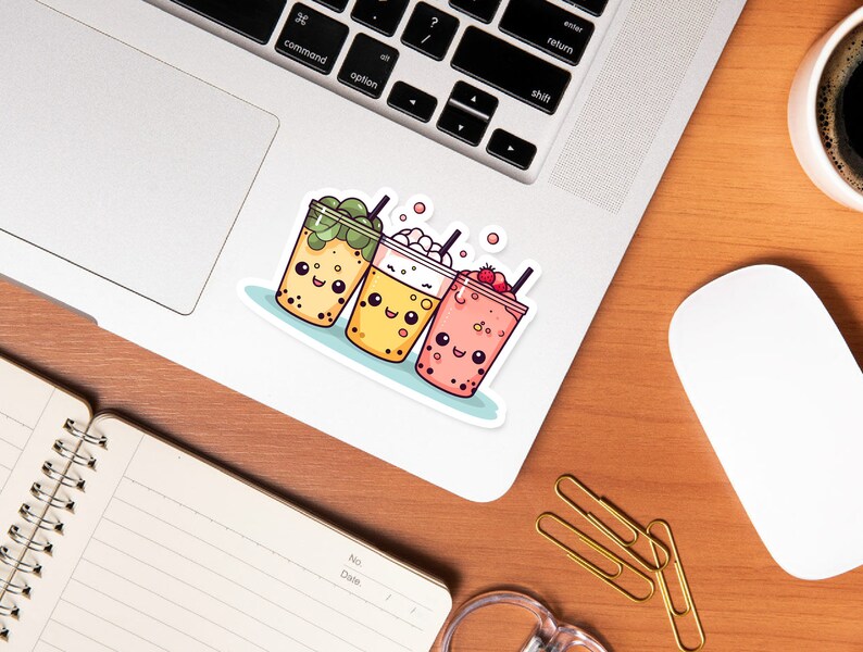 May include: A sticker depicting three cartoon bubble tea drinks with smiling faces. The drinks are in clear cups with various toppings: green tea, whipped cream, and strawberries. The sticker is on a laptop.