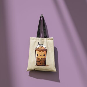 May include: A beige tote bag with black handles hangs against a purple wall. The bag features a cartoon illustration of a brown bubble tea drink with a smiling face. The drink has a clear lid and a straw.