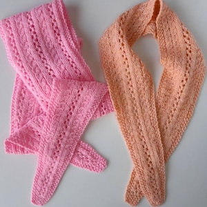 Könnte beinhalten: Zwei gestrickte Schals, einer hellrosa, der andere pfirsichfarben. Beide haben ein detailliertes Lochmuster. Die Schals sind aus weichem Garn, wahrscheinlich handgefertigt. Das Lochmuster verleiht den Schals eine zarte Note.