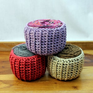 May include: Three crocheted yarn bowls in different colors. The top bowl is purple, the middle bowl is red, and the bottom bowl is beige.