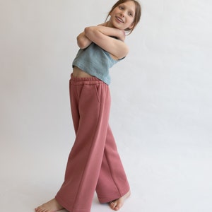 May include: A young person wearing a light blue sleeveless top and wide-legged, rose-colored pants. The pants have a drawstring waistband and a relaxed fit.