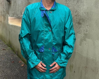 May include: A teal blue jacket with a zipper and button closure. The jacket has a drawstring waist and a blue lining. The model is wearing blue jeans.
