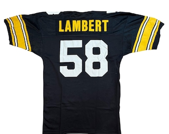 Pode incluir: Camisola de futebol preta com o nome "LAMBERT" em letras amarelas nos ombros e o número "58" em branco nas costas. As mangas têm riscas amarelas e brancas.