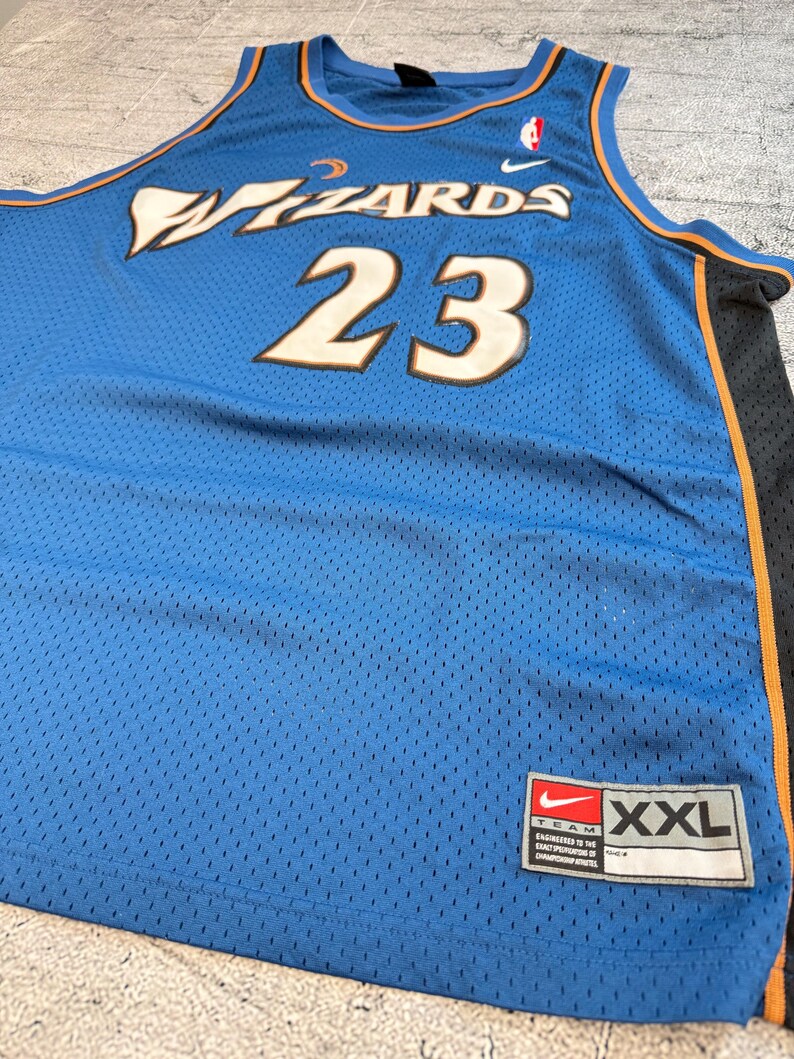 K&ouml;nnte beinhalten: Ein blaues Basketballtrikot aus Mesh mit dem Wort "Wizards" in wei&szlig;-goldenen Buchstaben und der Nummer "23". Das Trikot hat ein Nike-Logo und ein XXL-Etikett.