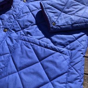 May include: A blue quilted jacket with a diamond pattern. The jacket has a zipper closure and two pockets.