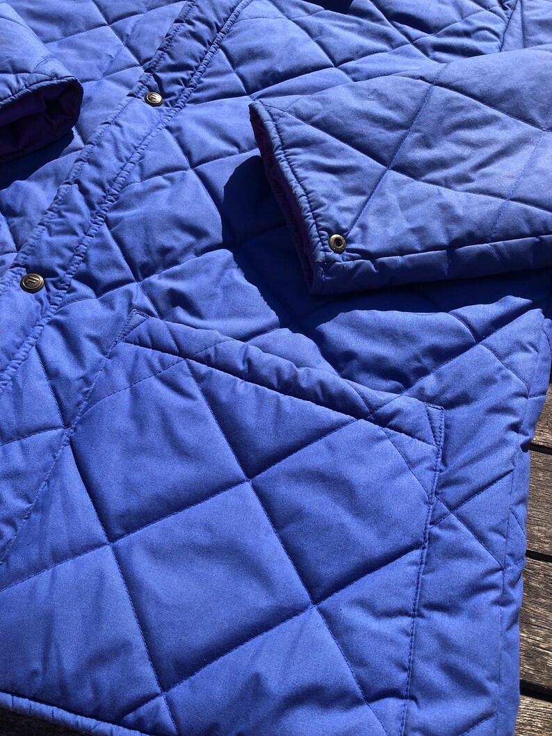 May include: A blue quilted jacket with a diamond pattern. The jacket has a zipper closure and two pockets.