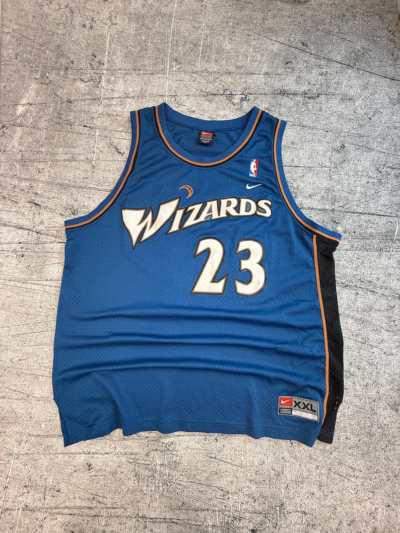 K&ouml;nnte beinhalten: Blaues Wizards-Basketballtrikot mit der Nummer 23 in Wei&szlig;. Das Trikot hat das Wizards-Logo auf der Vorderseite und ein Nike-Logo. Das Trikot ist in der Gr&ouml;&szlig;e XXL.