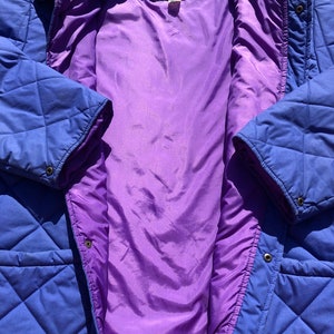 May include: A blue quilted jacket with a purple lining. The jacket has a zipper closure and a snap button closure. The label on the jacket reads "Aries".