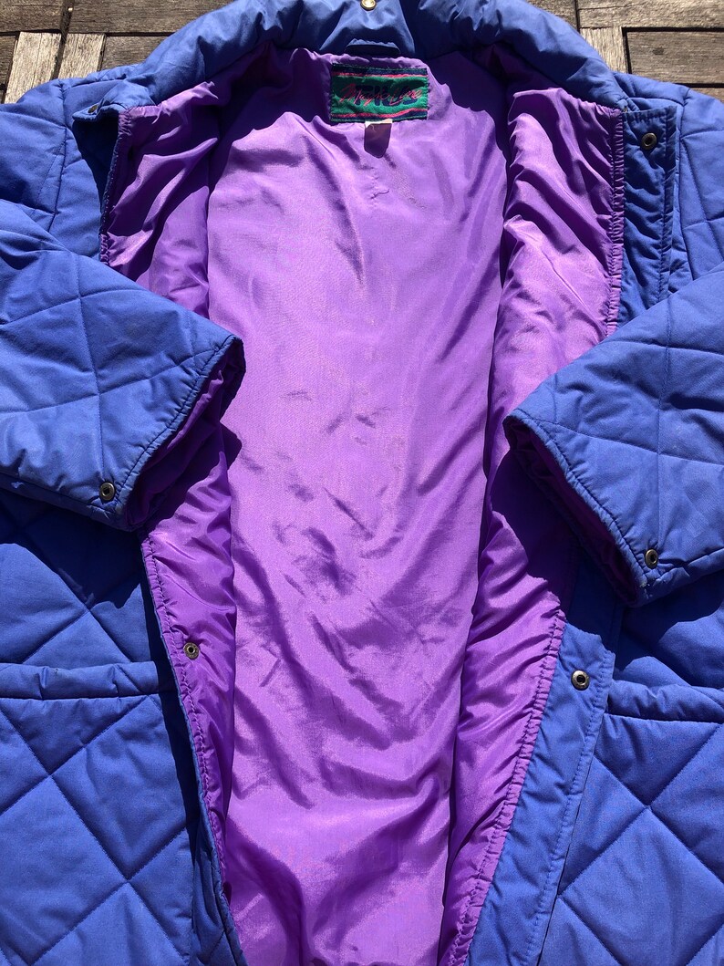 May include: A blue quilted jacket with a purple lining. The jacket has a zipper closure and a snap button closure. The label on the jacket reads "Aries".