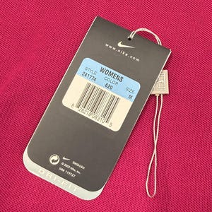 May include: A pink DRI-FIT shirt with a tag attached. The tag displays "WOMENS", style number 241774, color 620, and size M. The tag also includes the Nike logo and the text "www.nike.com".