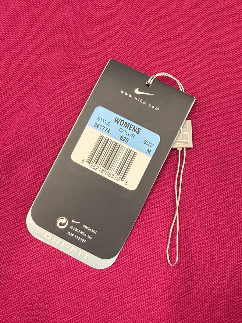 May include: A pink DRI-FIT shirt with a tag attached. The tag displays "WOMENS", style number 241774, color 620, and size M. The tag also includes the Nike logo and the text "www.nike.com".