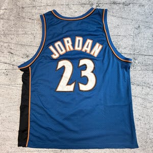 K&ouml;nnte beinhalten: Blaues Basketballtrikot mit dem Namen "JORDAN" und der Nummer "23" in Wei&szlig;. Das Trikot hat orangefarbene und schwarze Akzente. Das Trikot besteht aus einem Mesh-Material.