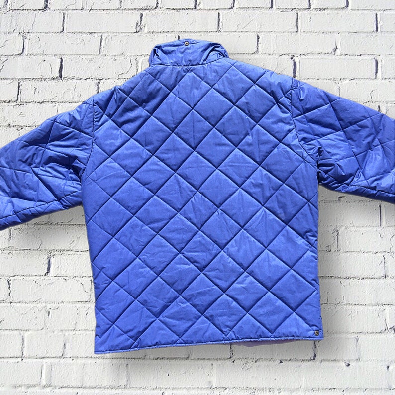 May include: A blue quilted jacket with a diamond pattern. The jacket has a high collar and a zipper closure.