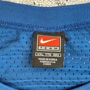 K&ouml;nnte beinhalten: Nahaufnahme eines blauen Mesh-Trikots mit einem schwarzen und roten Nike-Etikett. Auf dem Etikett steht "TEAM" mit dem Nike-Swoosh-Logo und "XXL TTG EEG". Das Trikot wird in Korea hergestellt.