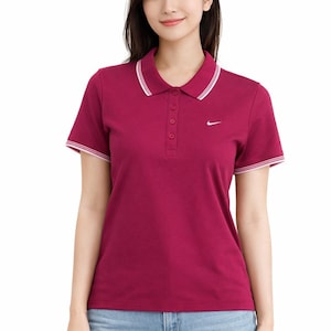 May include: A maroon polo shirt with a white collar and sleeve trim. The shirt has a three-button placket and a small white Nike logo on the chest. The model is wearing blue jeans.