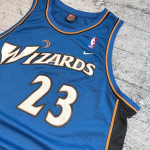 K&ouml;nnte beinhalten: Ein blaues Wizards-Basketballtrikot mit der Nummer 23 in Wei&szlig; mit kupferfarbener Umrandung. Das Trikot zeigt das Wizards-Logo und das NBA-Logo. Das Trikot hat eine Mesh-Textur und orangefarbene und schwarze Verzierungen.