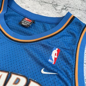 K&ouml;nnte beinhalten: Ein blaues Basketballtrikot mit orangefarbenen und schwarzen Zierleisten. Das Trikot zeigt das NBA-Logo, den Nike-Swoosh und das Wort "WIZARDS" in Wei&szlig;. Das Trikot hat einen V-Ausschnitt und besteht aus atmungsaktivem Material.
