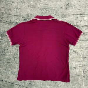 May include: A short-sleeved polo shirt in a deep magenta color. The shirt features a white collar and white trim along the sleeves. The back view of the shirt is shown, highlighting the classic polo design.