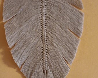 May include: A beige macrame feather wall hanging with a wooden bead at the top.