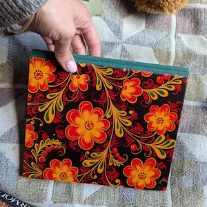 Puede incluir: Un cuaderno negro con un borde verde y un diseño floral colorido. Las flores son rojas, naranjas, amarillas y verdes. El diseño recuerda al arte popular ruso tradicional.