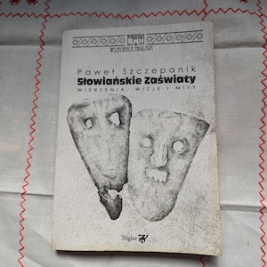 May include: A book cover featuring a black and white illustration of two masks. The book title is "Słowiańskie Zaświaty" and the author is "Paweł Szczepanik".