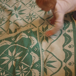Op de afbeelding: Een geweven deken in groen en wit met een geometrisch patroon. De deken is dubbelgevouwen en een kind speelt erop.