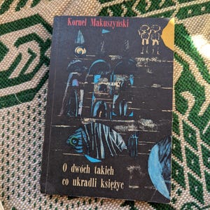May include: A vintage paperback book with a black cover and colorful illustrations. The title is "O dwóch takich co ukradli księżyc" by Kornel Makuszynski.