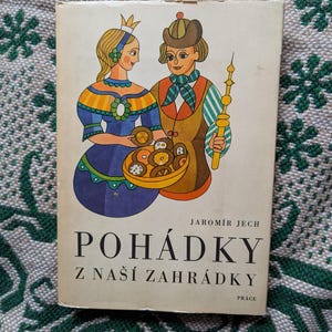 May include: Vintage book cover featuring a colorful illustration of a royal couple. The artwork depicts a woman in a blue dress and a man holding a staff. The title "POHÁDKY Z NAŠÍ ZAHRÁDKY" is prominently displayed.
