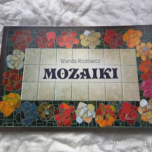 Puede incluir: Una portada de libro con un diseño de mosaico colorido con un borde floral. El título del libro es "MOZAIKI" de Wanda Rodowicz.