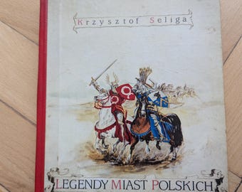 May include: A hardcover book with a red spine and a faded cover featuring illustrations of knights on horseback. The book's title, "Legendy Miast Polskich," is visible, along with the author's name, "Krzysztof Seliga."