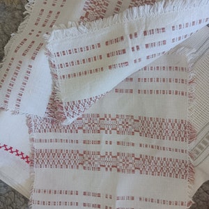 Puede incluir: Cuatro manteles individuales de lino blanco con un diseño tejido rojo. Los manteles individuales tienen un borde con flecos.