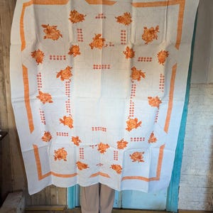 Puede incluir: Un mantel blanco con un patrón floral naranja. El mantel tiene un diseño geométrico con flores naranjas y puntos rojos.
